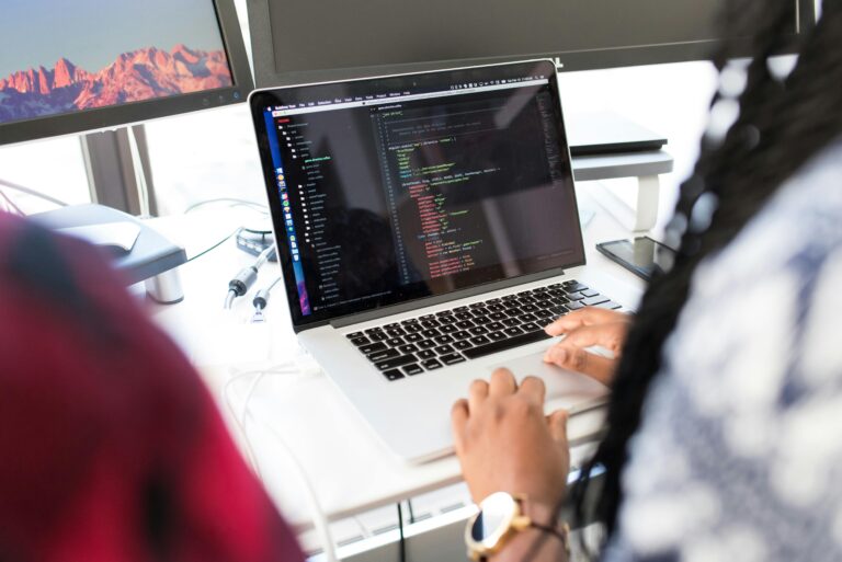 A woman coding on a laptop in a modern office environment with multiple monitors.